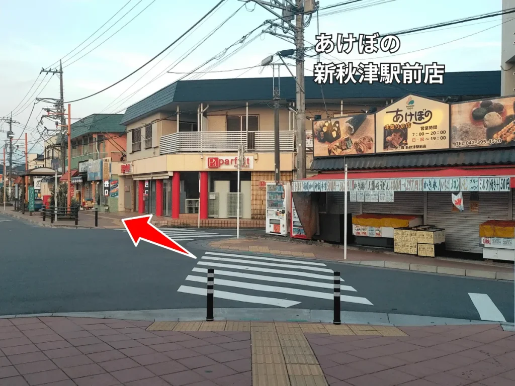 あけぼの新秋津駅前店前の交差点を左へ曲がる道順を示す赤い矢印。