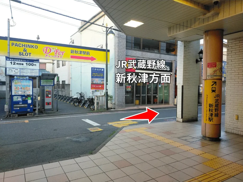 西武池袋線秋津駅南口を出て右へ。JR武蔵野線新秋津駅方面の看板と道順を示す赤い矢印。