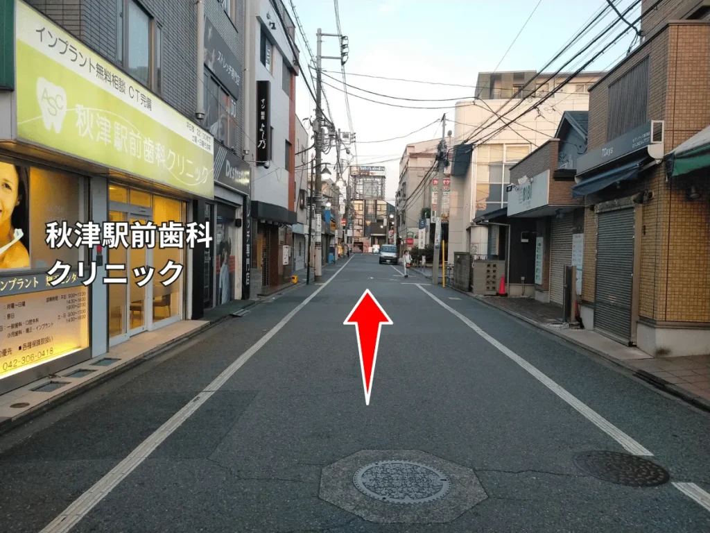 秋津商店街。秋津駅前歯科クリニックを過ぎてまっすぐ進む方向を示す赤い矢印。